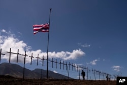 Crosses honoring the victims killed in a recent wildfire hang on a fence along the Lahaina Bypass as a Hawaiian flag flies in the wind in Lahaina, Hawaii, Aug. 22, 2023.