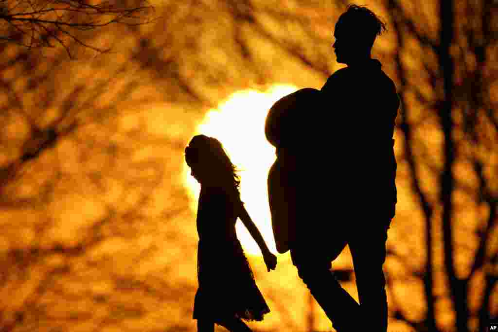 Siluet dua orang berjalan di taman saat matahari terbenam di hari dengan cuaca yang tidak biasanya hangat, di kota Kansas City, Missouri. (AP)&nbsp;