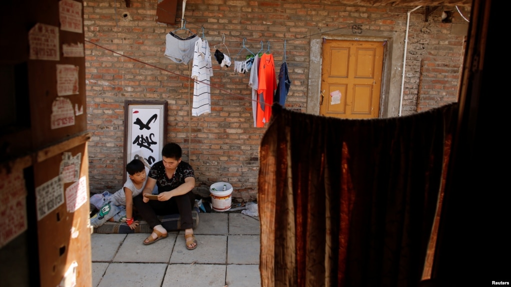 资料照：两个农民工的孩子在北京郊区东三旗村即将被拆除的农民工住宅区里使用手机。（2017年8月6日）(photo:VOA)