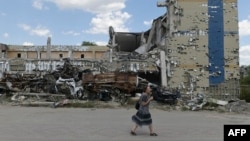 A woman walks past a destroyed building in Mariupol, Ukraine, Aug. 16, 2023, amid the Russian invasion of Ukraine. 