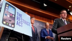 FILE: U.S. Senator Mark Warner (D-VA) speaks as U.S. Senator Joe Manchin (D-WV) looks on during a press conference to unveil legislation that would allow the Biden administration to "ban or prohibit" Chinese-owned video app TikTok, on Capitol Hill in Washington, Mar. 7, 2023.