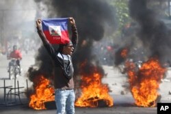 Seorang pengunjuk rasa mengibarkan bendera Haiti saat protes menuntut pengunduran diri Perdana Menteri Ariel Henry di Port-au-Prince, Haiti, Jumat, 1 Maret 2024. (Foto: AP)