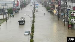 Orang-orang dan kendaraan berjalan melintasi jalan yang terendam banjir akibat Topan Gaemi di kota Kaohsiung, Taiwan, Kamis 25 Juli 2024.