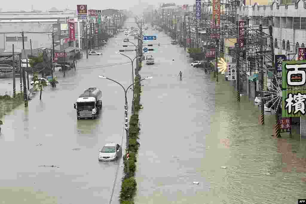 People and vehicles wade through the water along a street that was flooded by Typhoon Gaemi in Kaohsiung, Taiwan, July 25, 2024.&nbsp;The typhoon -- the strongest to hit Taiwan in eight years -- had already forced authorities on the island to close schools and offices, suspend the stock market and evacuate thousands of people.