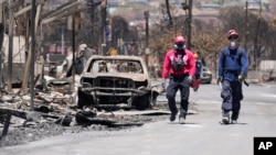Members of a search-and-rescue team walk along a street, Aug. 12, 2023, in Lahaina, Hawaii, following heavy damage caused by wildfire.