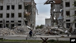 FILE - A local woman rides a bicycle on April 18, 2024, in front of a building destroyed by a Russian airstrike in the frontline town of Orikhiv, Ukraine. 