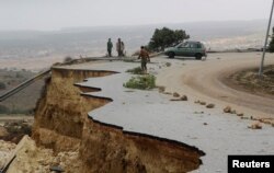 People stand in a damaged road as a powerful storm and heavy rainfall flooded hit Shahhat city, Libya, Sept. 11, 2023.