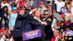 Le candidat républicain à la présidence, l'ancien président Donald Trump, est aidé à quitter la scène lors d'un événement de campagne à Butler, en Pennsylvanie, le samedi 13 juillet 2024. (AP Photo/Gene J. Puskar)