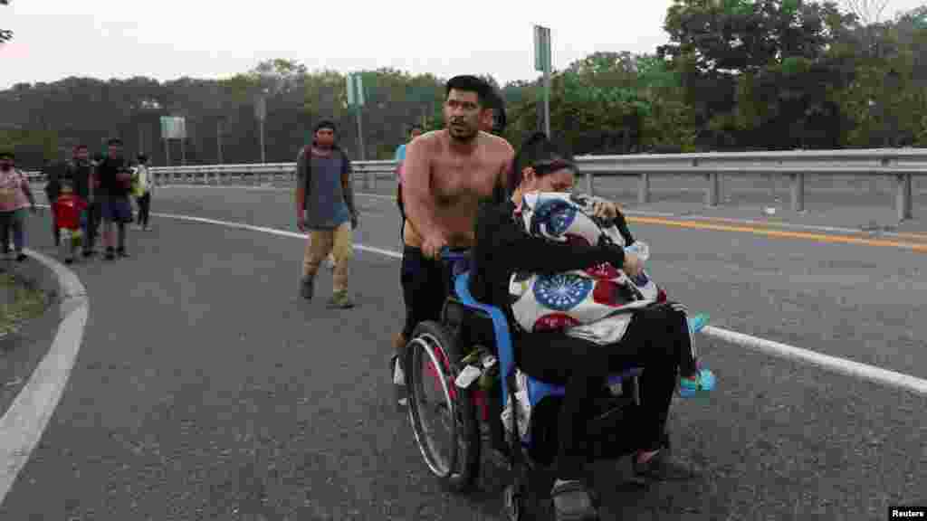 Un migrante empuja la silla de ruedas donde va una mujer con un niño pequeño. 