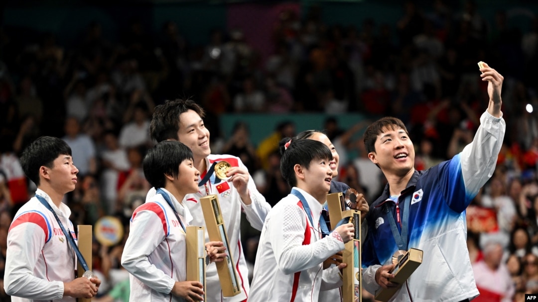 Bronze medalists S. Korea's Lim Jonghoon takes a selfie with: gold medalists China's Wang Chuqin and China's Sun Yingsha, silver medalists N. Korea's Ri Jong Sik, and N. Korea's Kim Kum Yong and bronze medalist Shin Yubin, July 30, 2024. 