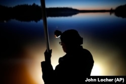 Headlamps light up the water as Mick Tainter holds a spear while fishing at the Chippewa Flowage on the Lac Courte Oreilles Reservation, April 14, 2024, near Hayward, Wisconsin. (AP Photo/John Locher)