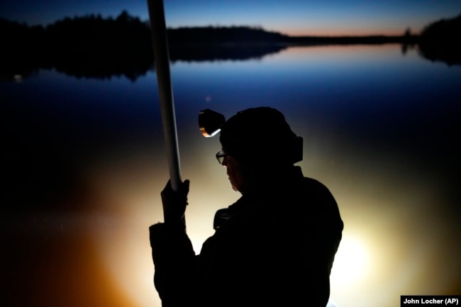 Headlamps light up the water as Mick Tainter holds a spear while fishing at the Chippewa Flowage on the Lac Courte Oreilles Reservation, April 14, 2024, near Hayward, Wisconsin. (AP Photo/John Locher)