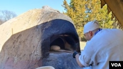 Chef Justin Cherry places his Colonial-style bread into the clay oven. Using a woodburning fire, he heats the oven for about five hours, which keeps it hot for some four hours, he said. (Deborah Block/VOA)