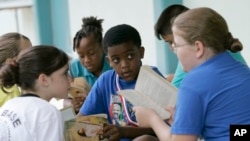 FILE - Joseph Webb, center, Kristina Carr, right, and Kaelyn Korovich, left, read outside their classroom at Air Base Elementary School, June 4, 2009, in Homestead, Fla.