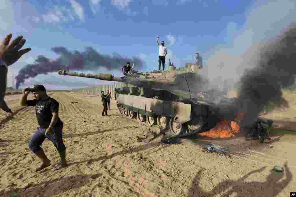 Palestinians celebrate at a destroyed Israeli tank at the Gaza Strip fence east of Khan Younis, Israel, Oct. 7, 2023.