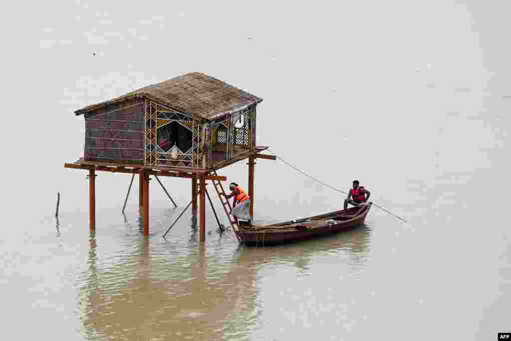 Men row a boat near a deluged straw hut in the river Ganges in Prayagraj, India, after rise in water levels during the monsoons.