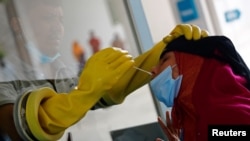 বাংলাদেশের রাজধানী ঢাকার মুগদা মেডিকেল কলেজ ও হাসপাতালে করোনভাইরাস পরীক্ষার জন্য এক মহিলার নাক থেকে সোয়াব সংগ্রহ করছেন একজন স্বাস্থ্যকর্মী। (ফাইল ছবি) 