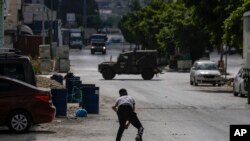 A Palestinian youth throws a stone at an Israeli military vehicle during an Israeli army raid in the Balata refugee camp near the West Bank town of Nablus, May 13, 2023.