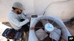 FILE - Total Refrigeration service tech Michael Villa works on replacing a fan motor on an air conditioner as temperatures were expected to hit 42.7 Celsius (117 Fahrenheit), July 19, 2023, in Phoenix, Arizona.