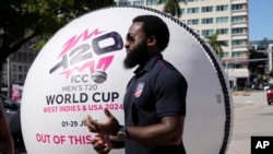FILE - Aaron Jones, vice-captain of Team USA, tosses a cricket ball as he stands next to a giant cricket ball at an event marking 100 days until the ICC men's T20 Cricket World Cup 2024 is held in the United States, Feb. 22, 2024, in downtown Miami.