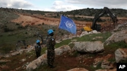 FILE - UN peacekeepers hold their flag as they observe Israeli excavators' attempt to destroy tunnels built by Hezbollah, near the southern Lebanese-Israeli border village of Mays al-Jabal, Lebanon on Dec. 13, 2019. 