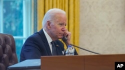FILE - In this photo taken through a window, President Joe Biden talks on the phone in the Oval Office of the White House in Washington, Dec. 9, 2021. Biden spoke with Chinese President Xi 