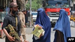 FILE - Afghan burqa-clad women walk past a Taliban security officer along a street in Jalalabad on April 30, 2023. 