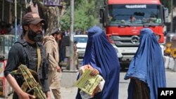 FILE - Afghan burqa-clad women walk past a Taliban security guard along a street in Jalalabad, in Taliban-ruled Afghanistan, April 30, 2023. 