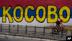 FILE - A man rides past a mural with the writing "Kosovo" and the colors of the Serbian flag in Belgrade, Serbia, on July 13, 2023. Kosovo is a former province in Serbia whose 2008 declaration of independence Belgrade does not recognize.
