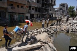 Warga Palestina berjalan di atas puing-puing bangunan yang hancur akibat pengeboman Israel sebelumnya, di antara dua genangan air, di Khan Yunis, selatan Jalur Gaza, pada 19 Juli 2024. (Foto: AFP)