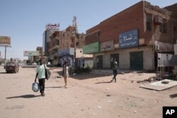 People walk past shuttered shops in Khartoum, Sudan, April 18, 2023.