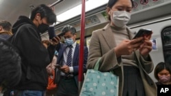 FILE - Commuters wearing face masks check their smartphones on a subway train in Hong Kong, Feb. 7, 2023. Hong Kong lifted its mask mandate March 1, 2023, ending the city’s last major restriction imposed during the COVID-19 pandemic.