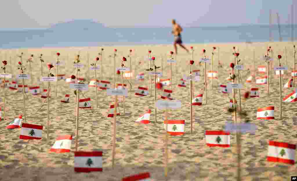 A man runs past Lebanese flags placed in honor of those who died in the 2020 Beirut port explosion on the third anniversary of the blast, on Copacabana beach in Rio de Janeiro, Brazil.