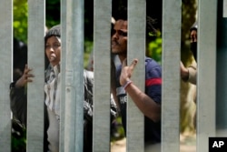 FILE - Migrants stand behind the metal barrier border that Poland has erected along the border with Belarus, in Bialowieza Forest, May 29, 2024.