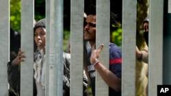 Migrants stand behind the metal barrier border that Poland has erected along the border with Belarus, in Bialowieza Forest, May 29, 2024.