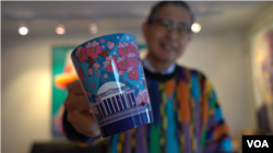 El artista salvadoreño Nicolás Shi posa con una taza que muestra su diseño