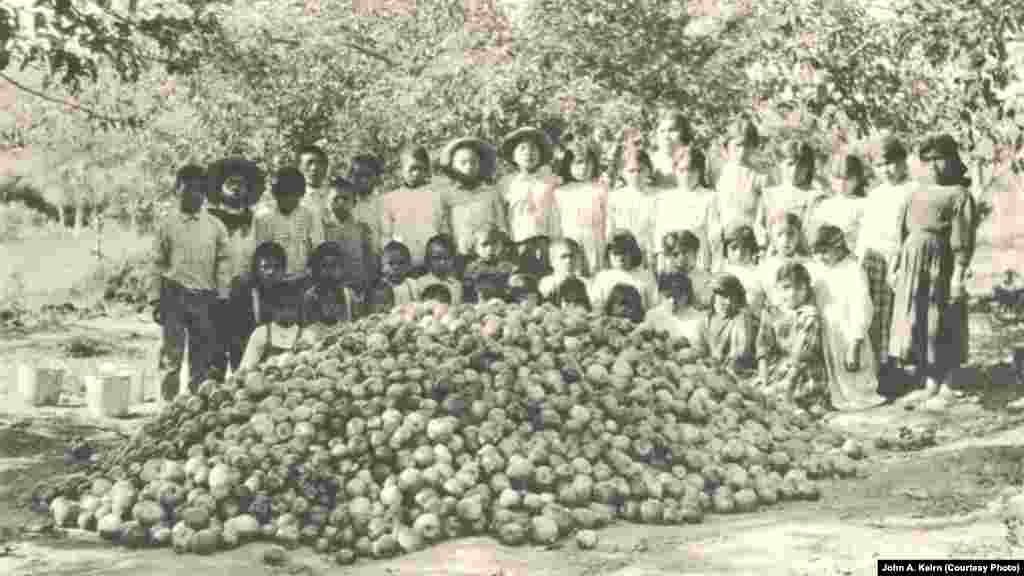In this undated photo taken by John A. Keirn, Indian school students pose behind a mound of apples they have picked.