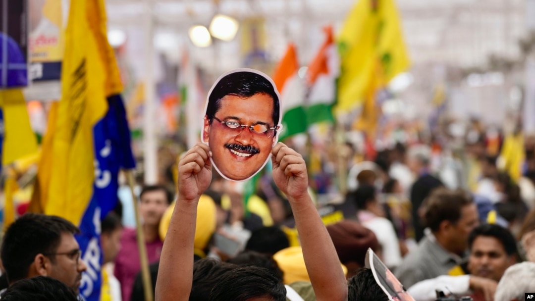 Seorang pendukung Partai Aam Admi memegang topeng yang mirip dengan pemimpin partai dan Ketua Menteri Delhi Arvind Kejriwal saat berdemonstrasi di New Delhi, India, Minggu, 31 Maret. 2024. (Foto: AP)