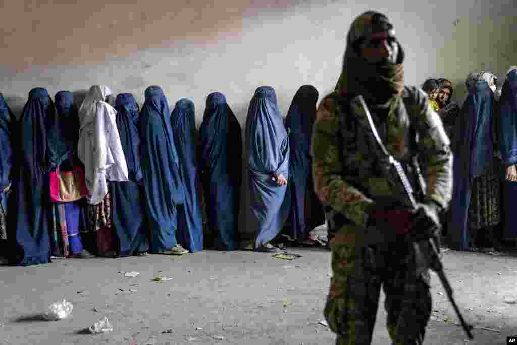 A Taliban fighter stands guard as women wait to receive food rations distributed by a humanitarian aid group, in Kabul, Afghanistan.