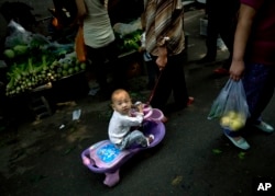 FILE - Seorang perempuan menarik sepeda mini yang dinaiki balitanya, melalui pasar pagi di sepanjang gang Hutong di Beijing Minggu, 9 September 2012. (Andy Wong/VOA)