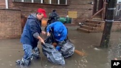 Nesta fotografia tirada de um vídeo, duas pessoas trabalham nas águas das cheias para desobstruir os esgotos numa rua, sexta-feira, 29 de setembro de 2023, no bairro de Brooklyn, em Nova Iorque