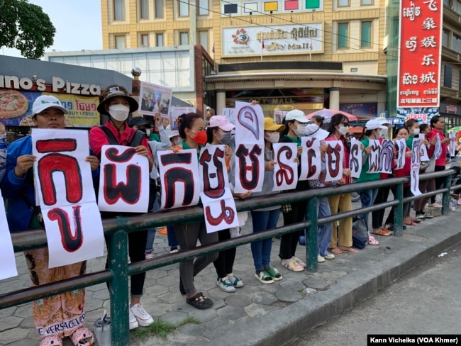 រូបឯកសារ៖ ក្រុមបុគ្គលិក និងសហជីពណាហ្គាវើលដ៍ ឈរលើកបដា និងរូបថត គាំទ្រថ្នាក់ដឹកនាំសហជីពរបស់ខ្លួន នៅខឿនផ្លូវម្ខាងទៀតពីមុខតុលាការ នៅថ្ងៃទី២៥ ខែឧសភា ឆ្នាំ២០២៣ ក្នុងអំឡុងការប្រកាស​សាលក្រម​រឿងក្តីរបស់កញ្ញា ឈឹម ស៊ីថរ។ (កាន់ វិច្ឆិកា/វីអូអេ)
