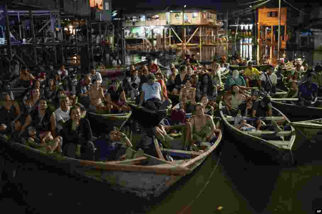 Spectators sit on boats watching a film projected on a screen set up on a wooden structure during the Muyuna Floating Film Festival in the Belen neighborhood of Iquitos, Peru, May 25, 2024.