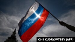 Seorang pria mengibarkan bendera nasional Rusia pada 11 Juni 2023. Polandia pada Rabu (22/11) mengatakan bahwa pihaknya telah mendakwa 16 orang asing sebagai mata-mata untuk Rusia (Foto: AFP/Kirill KUDRYAVTSEV)