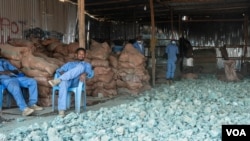 刚果民主共和国东南部科卢韦齐附近卡米隆贝矿场的一个矿石贸易仓库的一名员工坐在一排排含有铜和钴的孔雀石旁边。 （2023年6月20日）