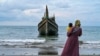 A woman with her child looks at a boat which carried Rohingya refugees to the Laweueng beach in Pidie district of Aceh province, Indonesia, Dec. 10, 2023. 