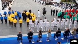 Lieutenant General and Military Governor of Paris Christophe Abad holds the Olympic flame torch on a horse as he does the torch kiss with a torch bearer during the Bastille Day military parade along the Avenue Foch, in Paris, July 14, 2024. 