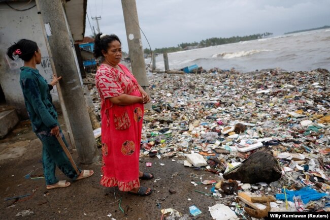 Solikah, 58, dan Cartini, 35, mengamati sampah, sebagian besar plastik dan sampah rumah tangga, yang menutupi pantai di lingkungan mereka di desa nelayan Teluk, Pandeglang, Banten, Maret 15, 2024. (Foto: REUTERS/Willy Kurniawan)