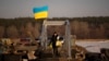 A woman crosses a makeshift pedestrian bridge connecting the two sides of a destroyed road bridge in Staryi Saltiv, Ukraine, Feb. 17, 2023.