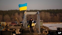 A woman crosses a makeshift pedestrian bridge connecting the two sides of a destroyed road bridge in Staryi Saltiv, Ukraine, Feb. 17, 2023.